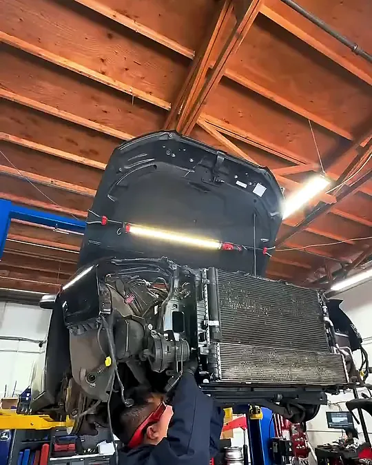 Audi front-end assembly with the radiator stack hanging on the lift under the shop's wood ceiling