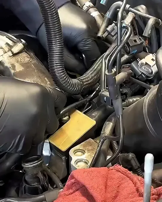 Gloved hands working deep in the Audi V6 engine bay beside a red shop rag