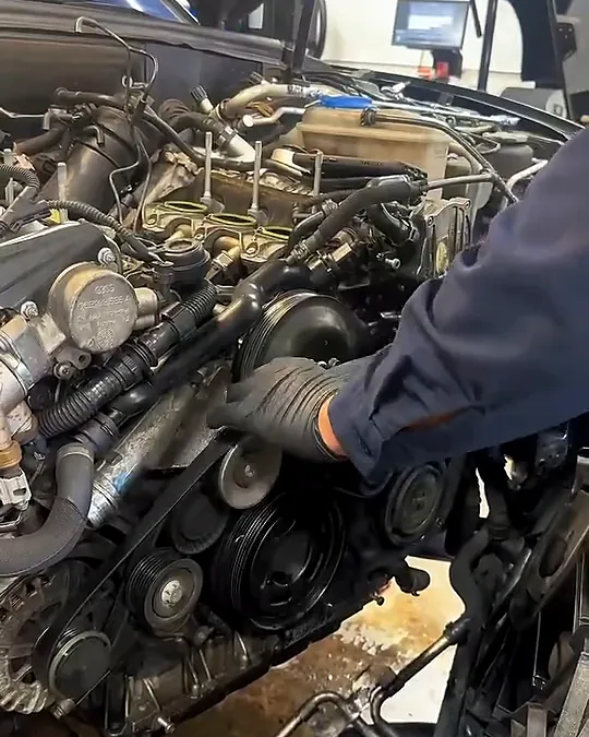 Technician's gloved hand on the front of the Audi V6 next to the belts and pulleys